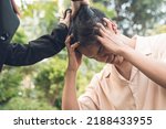 Small photo of A livid young woman pulls her boyfriend's hair out of rage and intense jealousy. A possessive and physically abusive girlfriend. Outdoor scene.