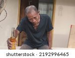 Small photo of A barely conscious and drunk middle aged asian man mumbling in slurred speech while trying to offer his drink. Tipsy and inebriated with alcohol.