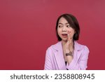 Small photo of A chatty young asian woman in her mid 20s spreading hearsay or gossip secretly. Wearing a pink blazer and black tube top. Studio shot with burgundy background.