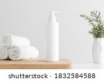 White cosmetic shampoo dispenser bottle mockup with towels and a rosemary  on a wooden table.