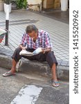 Small photo of Malaysia,May 24, 2019:Man reads a newspaper on footpath at Penan