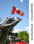 Small photo of Ottawa, Canada - May 24 2009 - A statue named named Territorial Prerogative of a grizzly bear eating a fish with a Canadian flag in the background. It was sculpted by Bruce Garner.