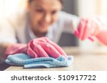 Woman in protective gloves is smiling and wiping dust using a spray and a duster while cleaning her house, close-up