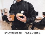 Police officers eat donuts and drink coffee at the police station. They rest in the break of work. They are in a good mood, they are smiling.
