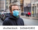 Handsome young European man in winter clothes on the street with a medical face mask on. Closeup of a 35-year-old male in a respirator to protect against infection with influenza virus or coronavirus