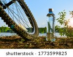 A bottle of clean water and a Bicycle wheel on the background of the lake shore. Rest after exercise on a summer evening.