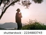 A young man peacefully meditates at sunset in a garden overlooking the mountains and the sea. A Caucasian guy does yoga in simple asanas on a viewpoint in the sunset sunlight