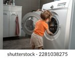 Small photo of One girl small caucasian toddler child daughter standing at the washing machine in the toilet opening or closing the door examine and learn early development and growing up mischief concept copy space
