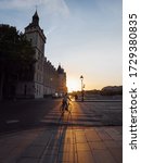 Small photo of A young girl rides a bicycle on a pedestrian crossing on a cobbled street of the Menial Bridge in Paris amid stunning sunset. Beautiful sunset in Paris.