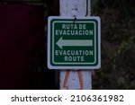 Sign in Spanish and English evacuation route with a direction arrow. Safety, danger, natural disaster concept.