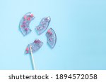 Broken in pieces transparent candy with little hearts on a stick. Smashed lollipop with sprinkles on blue background. Confectionery Topping. Unhappy love concept