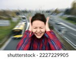 Small photo of Woman with closed eyes covering her ears in the street while vehicles are passing by fast in the background. Stressful and frustrating situation. Noise pollution concept. Radial blur filter applied.