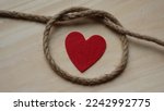 Small photo of Red heart in rope cord loop on wooden background. Symbol. Dependent relationship. Codependence. Abuse. Emotional trap. Social problem, message, psychology. - 10 January 2021, Montreal, Canada
