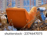 Small photo of An old armchair on the garbage heap of the city dump in the background of residential building. Household unsorted garbage in urban environment. Spontaneous unauthorized dumping. Ecological problem