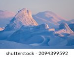 Winter arctic landscape. Ice hummocks and snowdrifts against the background of blurred mountains. Snow-covered ice floes close-up. Cold frosty winter weather. Polar region. Shallow depth of field.