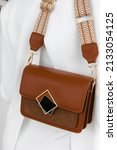 Small photo of Girl holding her handbag, close-up. Small fashionable women's leather clutch bag with fabric strap in shoe tone. Girl's Traditional clutch bag with brooch. handbag made of fine coloured genuine leathe