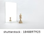 the king is reflected in the mirror as a pawn on white background. underestimation of their abilities