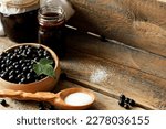 Small photo of black currant berries in a wooden dish on a wooden table with a jar of jam, a wooden spoon with sugar, concatenation of preparations for the winter, healthy food
