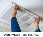 Small photo of Man opening ceiling air vent to replace dirty HVAC air filter. Home air duct system maintenance for clean air.