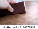 Small photo of Human hand with sandpaper on a copper background. Sanding of metal. The graininess of the sandpaper.