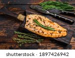Baked trout fillet on a cutting board. Dark wooden background. Top view.