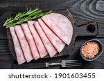 Sliced prosciutto ham on wooden cutting board. Black wooden background. Top view.