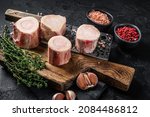 Small photo of Uncooked Raw veal Marrow bones on butcher board with meat cleaver. Black background. Top view