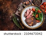 Small photo of BBQ Grilled rib eye steak, fried rib-eye beef meat on a plate with green salad. Dark background. top view. Copy space