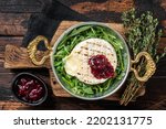 Baked Camembert Brie cheese with a cranberry sauce and garnished with arugula salad in a skillet. Wooden background. Top view.