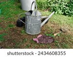 Small photo of A well used pair of gloves sit with a trowel and metal watering can on the lawn. Perhaps the gardener has gone in for a cup of tea?