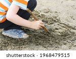 Small photo of Children's outdoor games. The child is squatting and playing with a stick in the mud.