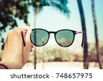 The girl is holding sunglasses in her hand against the background of blurry palms. Travel concept