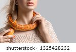 Small photo of Young, beautiful, woman with snake around her neck on grey background with copy space. Double-cross, foul play, perfidy, betrayal, treachery concept. False friendship. Judas. Stab in the back.