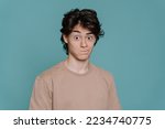 Small photo of Close up portrait of surpised schoolboy in beige t-shirt standing against turquoise studio backdrop with wide opened eyes. Mockup, perplexed guy looks at camera in wondering. Promo, sale, discount.