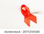 Small photo of Health care and medicine concept. AIDS awareness. Red AIDS awareness ribbon pierced with injection syringe on white background. Drug addiction and transmission of immunodeficiency virus through Spitz