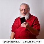 Small photo of Old man in bright red shirt with long white beard reacting to his cellphone as he reads his job just got the ax. Now that he lost his dead end job he will have to go on the dole.