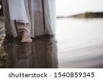 A closeup shot of a person wearing a biblical robe walking in the water near the shore