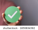 A hand holding a green paper with the checkmark sign on it