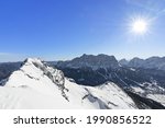 View from top of a mountain to Zugspitze (highest mountain of Germany) at a beautiful day in winter  Wild alpine landscape with sun and blue sky  Tiro