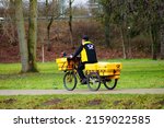 Small photo of FRANKFURT, GERMANY - Dec 30, 2021: A postman uses the cycle path along the river Nidda in Frankfurt to deliver his mail Yellow glow on a gloomy day Dynamic motion blur