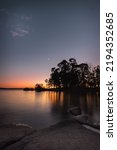 A vertical shot of a waterscape during sunset with trees and a beautiful skyline in the background