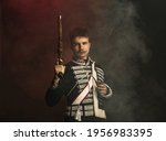 Small photo of Duelist. Young man in suit as royal person isolated on dark green background. Retro style, comparison of eras concept. Beautiful male model like historical character, monarch, old-fashioned.