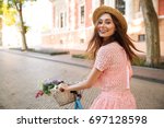 Smiling happy girl in dress and hat riding retro bicycle on a city street and looking at camera