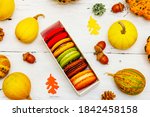 French macarons in autumn colors. Halloween dessert, Thanksgiving menu. Decorative pumpkins, fall leaves and acorns. White wooden boards background, top view