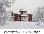 Snowfall in the village. Blurred background. Old wooden house in the snow. Traditional typical Scandinavian Swedish house or villa in the countryside in winter. Red cottage under snow flakes.