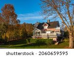 Small photo of Traditional scandinavian red old wooden house villa cottage with balcony in countryside. Beautiful glass veranda terrace bay window, alcove. Green hedge surrounded it. Pennant. Autumn fall season.