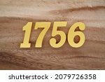 Small photo of Golden Arabic numerals 1756 on a dark brown to white wood grain background.