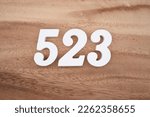 Small photo of White number 523 on a brown and light brown wooden background.