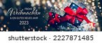 Small photo of Christmas greeting card with text in German - Frohe Weihnachten means Merry Christmas and Happy New Year 2023 - Gift box with red bow and bokeh lights