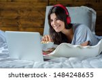 Young woman using laptop, eating popcorn and watching movies in bed at home.